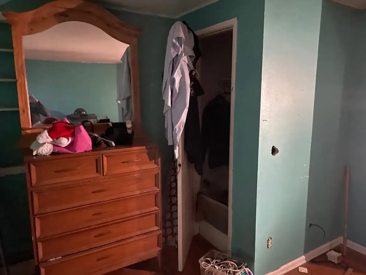 Selling a house during a divorce in Centereach: teal bedroom with a dresser and clothes piled up